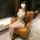 Woman in sheer mesh bodysuit and mini skirt set, featuring lace details and gold accents, seated on a leather chair.