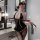 Woman in black pvc lace bodysuit with gold trim, holding a whip, styled as an airline stewardess costume for role play.