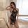 Woman wearing black sheer lace cheongsam lingerie set with split sides and halter neck, posing seductively by window.