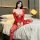 Woman wearing red sheer lace open-crotch bodysuit with floral embroidery and tear-away design, seated on bed.