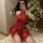 Woman in shiny red pu lace-up halter devil costume with batwing sleeves and sheer mini skirt, posing by christmas tree.