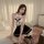 A woman poses elegantly in a black and white maid-themed bodysuit with lace details, featuring a plunging neckline and thigh-...