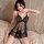 Woman wearing black lace sleepwear set with sheer slip dress, posing on bed in elegant bedroom setting.