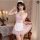 Woman modeling pink lace maid outfit with white apron and headpiece, featuring built-in pads, in elegant bedroom setting.