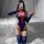 Woman in spider-man cosplay bodysuit with open-crotch design, posing on a bed with white drapes.