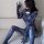 Woman in black spider-man cosplay costume with open-crotch design, posing seductively on couch.