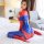 Woman in red and blue spider-themed sexy bodysuit with open-crotch design, posing on a bed for adult role play.