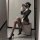 Woman in striped secretary outfit posing seductively on checkered stool, wearing high heels and sheer stockings.