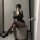Woman in striped sexy secretary outfit with black stockings and heels, posing seductively on checkered stool.