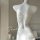 White sheer lace bodysuit with crisscross back straps, displayed on a mannequin in a soft-lit bedroom setting.