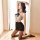 A woman poses elegantly in a black lace sleep dress with a bow detail, featuring a halter neck design and thigh-high stocking...