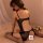 Woman wearing black sheer lace bodysuit with open back, cutouts, and fishnet stockings on bed.
