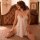Woman wearing white suoqing lace chemise nightgown with adjustable straps and high-slit design, sitting on bed.