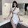 A woman poses elegantly in a chic kitchen, wearing a stylish white cheongsam-inspired dress featuring a high slit and black b...