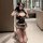 A woman poses in a bathroom wearing a black corset-style bodysuit with plaid skirt, fishnet stockings, and gloves, capturing ...