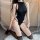 Woman wearing black suoqing open-crotch bodysuit with sheer panels and thigh-high stockings, kneeling on white rug.