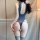 Woman wearing a grey open-crotch bodysuit with sheer panels and striped thigh-high stockings, posing in front of a dotted tul...