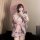 A person wearing a pink floral yukata robe with satin trim, bow detail, and embroidery, holding an umbrella while taking a se...
