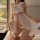 A woman poses on a bed wearing a sheer mesh babydoll dress with lace details, featuring a large bow at the chest and side sli...