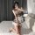 A person poses on a bed wearing a plaid maid costume dress with lace details, perfect for cosplay or date night outfits.