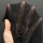 A hand holds a black twill lace garment, showcasing its intricate mesh design and delicate texture. the piece features a shee...
