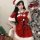 A festive woman poses beside a christmas tree wearing a red velvet robe with white fur trim and a santa hat, perfect for holi...