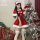 A festive woman poses beside a decorated christmas tree wearing a vibrant red velvet santa outfit, complete with a santa hat ...