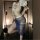 Woman wearing vintage chinese-inspired lace see-through cheongsam lingerie set, holding a floral fan in a modern hallway sett...