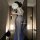 Woman wearing vintage chinese-inspired lace see-through cheongsam lingerie set, holding a fan in a modern hallway.