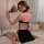 Woman in black velvet cheongsam lingerie with high slit, holding fan, seated on bed.