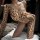Woman wearing a sexy wild leopard print bodysuit, a one-piece lingerie sleepwear set, posing on a white pillow.