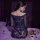 Woman in blue lace bodycon skirt set with sheer sleeves, sitting on bed with rose petals for date night.