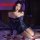 Woman wearing a sheer navy lace bodycon skirt set with long sleeves, posing on a bed with rose petals for date night or role ...