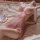 Woman in pink lace babydoll dress with push-up bra, sheer fabric, underwire support, lying on bed beside ornate mirror.