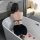 Woman in black velvet corset dress with high slit, sitting in bathtub with rose petals.