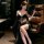 Woman in black luxury womens sensual lingerie set with fringe, sheer sleeves, and gold accents, holding a feather fan while s...