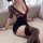 Woman wearing black lace bodysuit with floral sheer sleeves and halter neck, paired with thigh-high stockings, seated on a be...