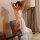 Woman wearing white lace bodysuit with sheer mesh skirt, posing on chair in elegant lingerie set for date night.