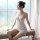 A woman sits by a window wearing a delicate white lace sleep dress with an embroidered design, featuring adjustable straps pe...