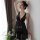 Woman wearing a black sheer lingerie set with lace details, posing elegantly by a window with soft lighting and flowers nearb...