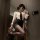 Woman in white blouse, black tie, mini skirt, and sheer stockings posing by a door.