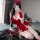 Woman wearing festive red christmas-themed lingerie set with bow headband, posing on rug indoors.