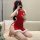 A woman poses on a couch wearing a festive red christmas-themed cheongsam outfit. the dress features sheer bust coverage, whi...