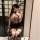 Woman in purple yaqin lingerie set with floral top, pencil skirt, and thigh-high stockings posing for mirror selfie.