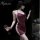 Woman wearing yaqin nu burgundy sleep dress with high slit, holding wine glass in dimly lit room.