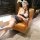 Woman in yaqin nu sexy lingerie set with striped mini skirt, top, and lace accessories, posing on a leather chair.