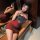 A woman poses elegantly in a sheer black top adorned with red roses and a form-fitting red bodycon skirt, creating a sexy and...