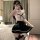 A woman poses in a mirror wearing a white crop top with black lace detailing and a black pleated skirt, paired with stockings...