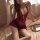 Woman wearing yueli lace bodysuit – sexy open-crotch sleepwear with minimalist modest design, in rich red lace on soft bed.