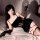 A woman poses on a bed wearing a black ziqu sexy velvet bodycon dress with lace trim, paired with matching stockings and glov...